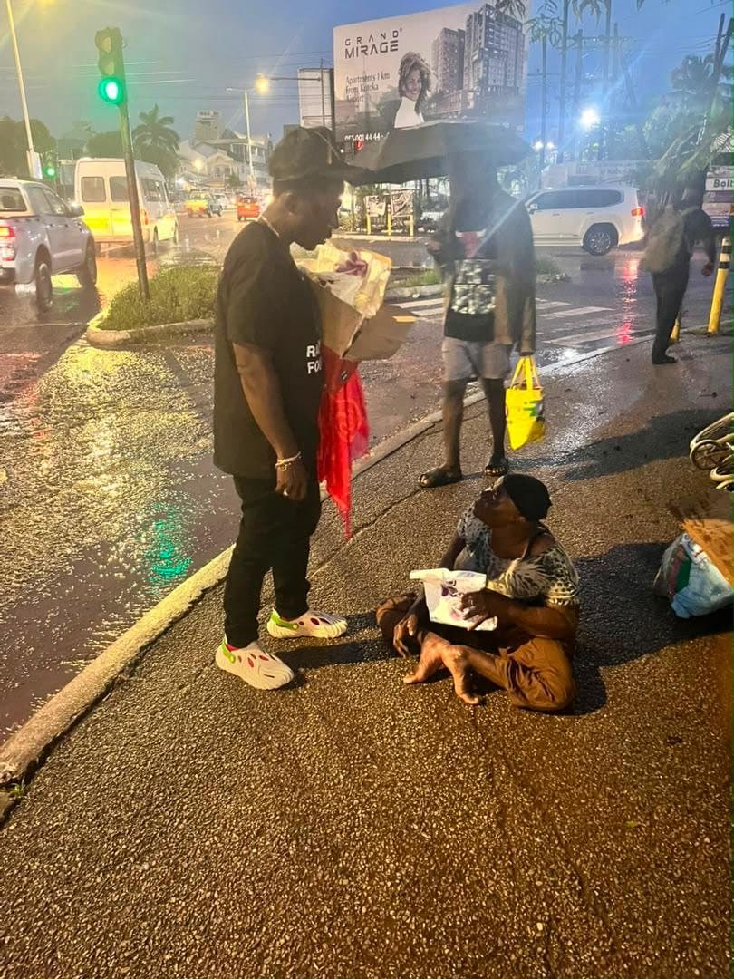 A volunteer handing a meal to a woman on a rainy street in Accra